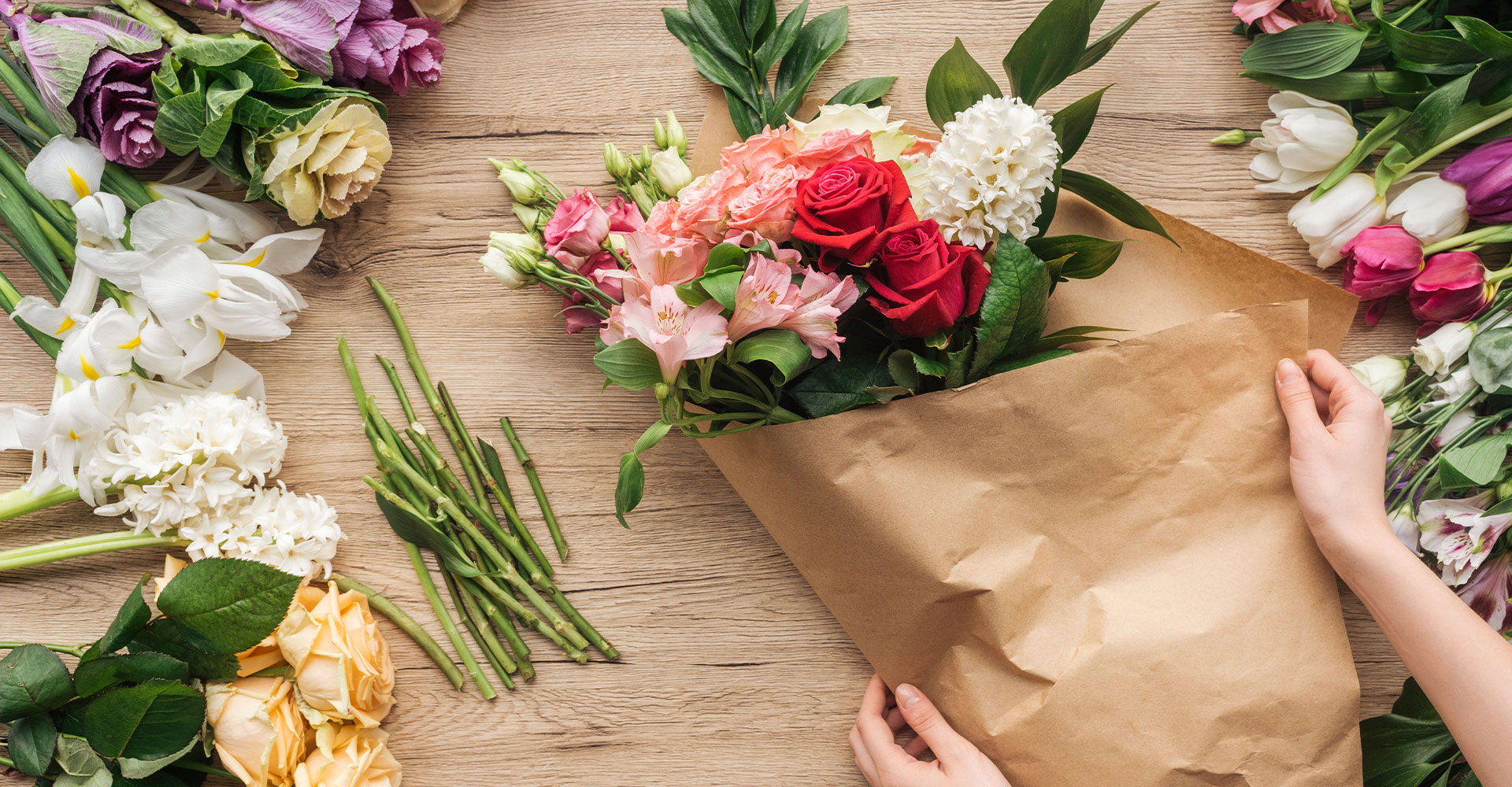 Auf einem Arbeitstisch liegen verschiedene Blumen. Ein Blumenstrauß wird gerade eingepackt.